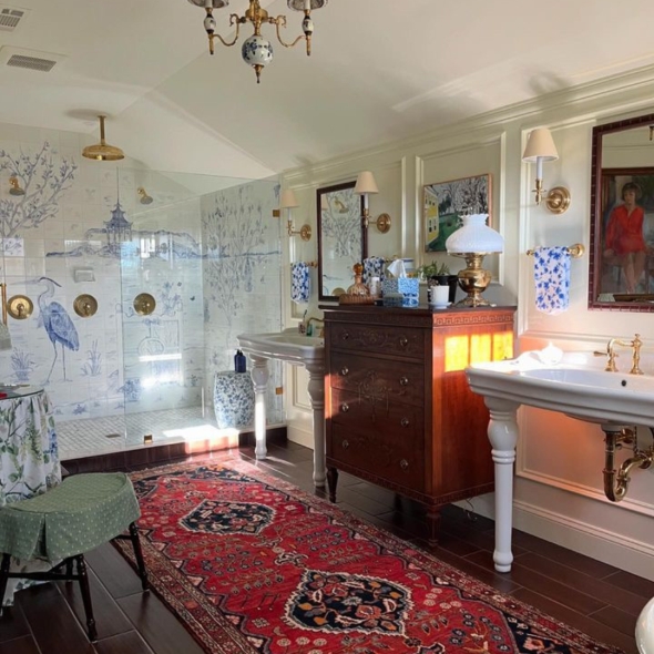 A spacious bathroom with a black clawfoot tub, floral curtains, a Persian-style rug, and a large white sink.  | BRG